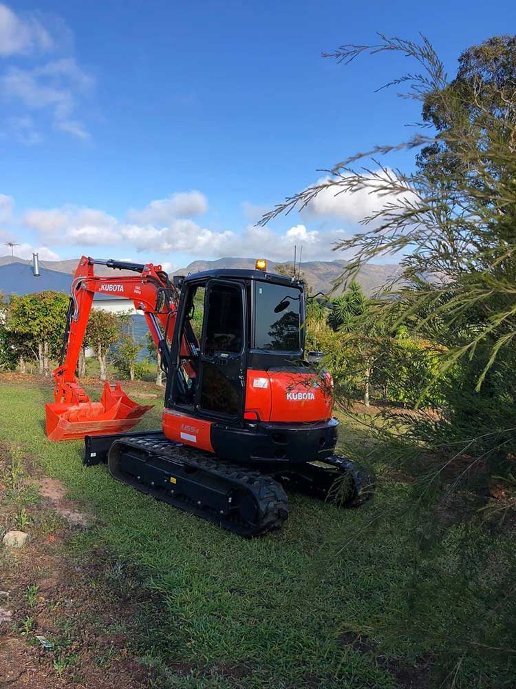 A Red and Black Excavator is Parked in a Grassy Field — Blue Gum Earthworks in Atherton, QLD