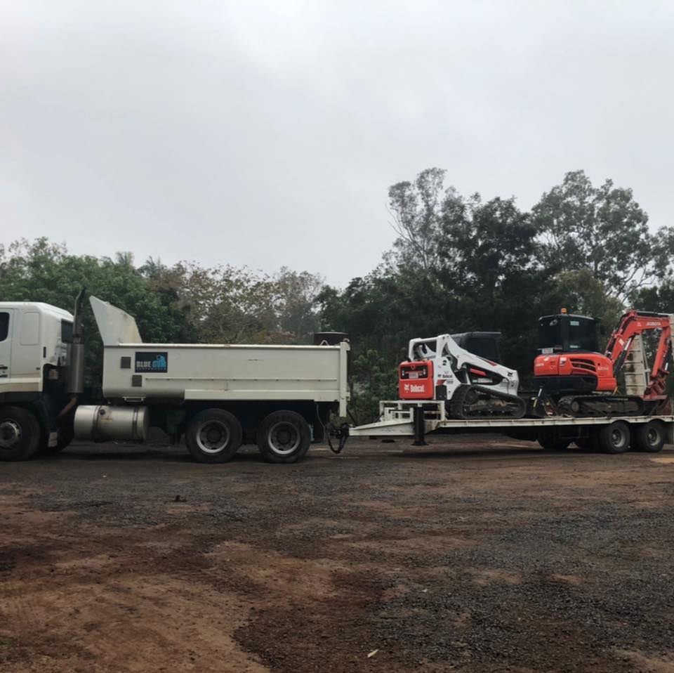 A Dump Truck is Towing a Small Excavator on a Trailer — Blue Gum Earthworks in Atherton, QLD