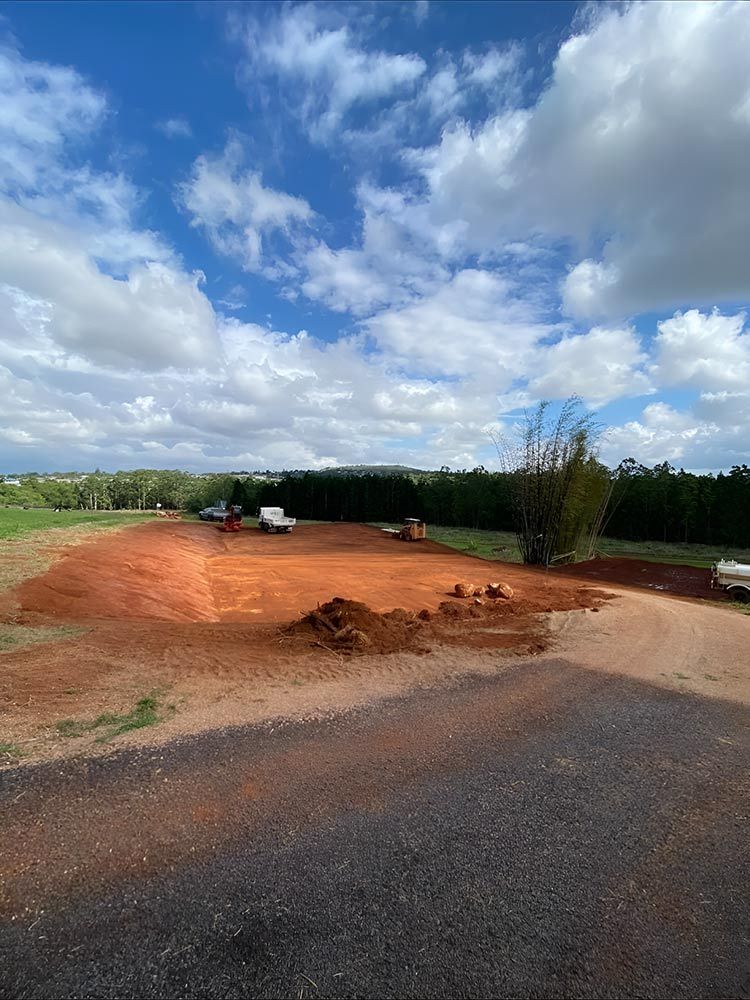A Dirt Road Going Through a Field With a Blue Sky and Clouds in the Background — Blue Gum Earthworks in Atherton, QLD