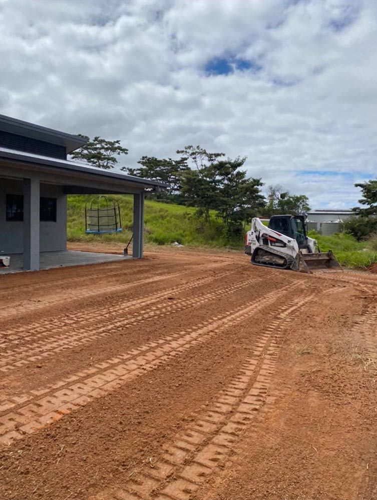 A Bulldozer is Driving Down a Dirt Road in Front of a House — Blue Gum Earthworks in Atherton, QLD
