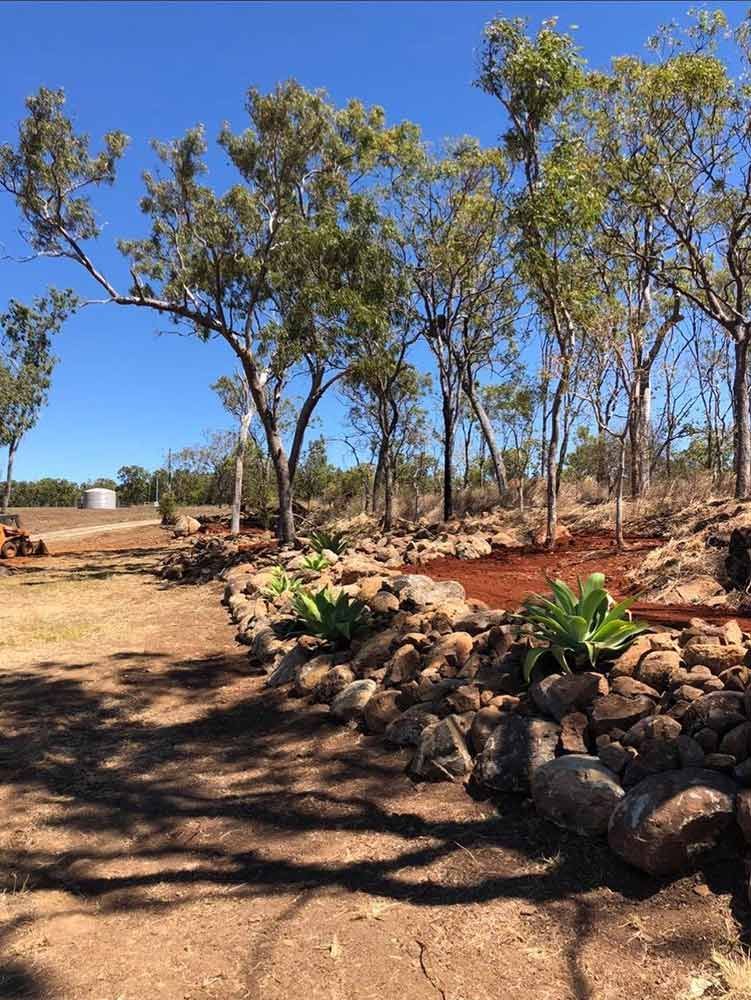 A Rock Wall Surrounded by Trees in a Field With a Blue Sky in the Background — Blue Gum Earthworks in Atherton, QLD