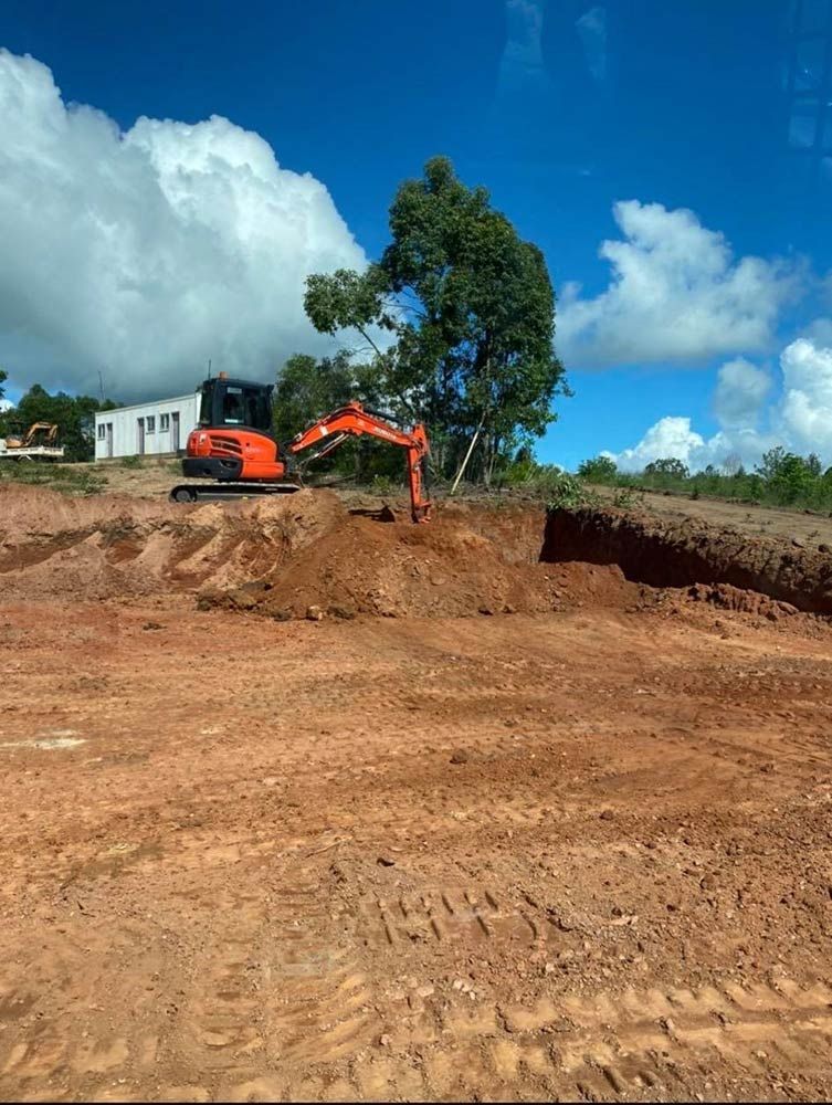 An Orange Excavator is Digging a Hole in a Dirt Field — Blue Gum Earthworks in Atherton, QLD