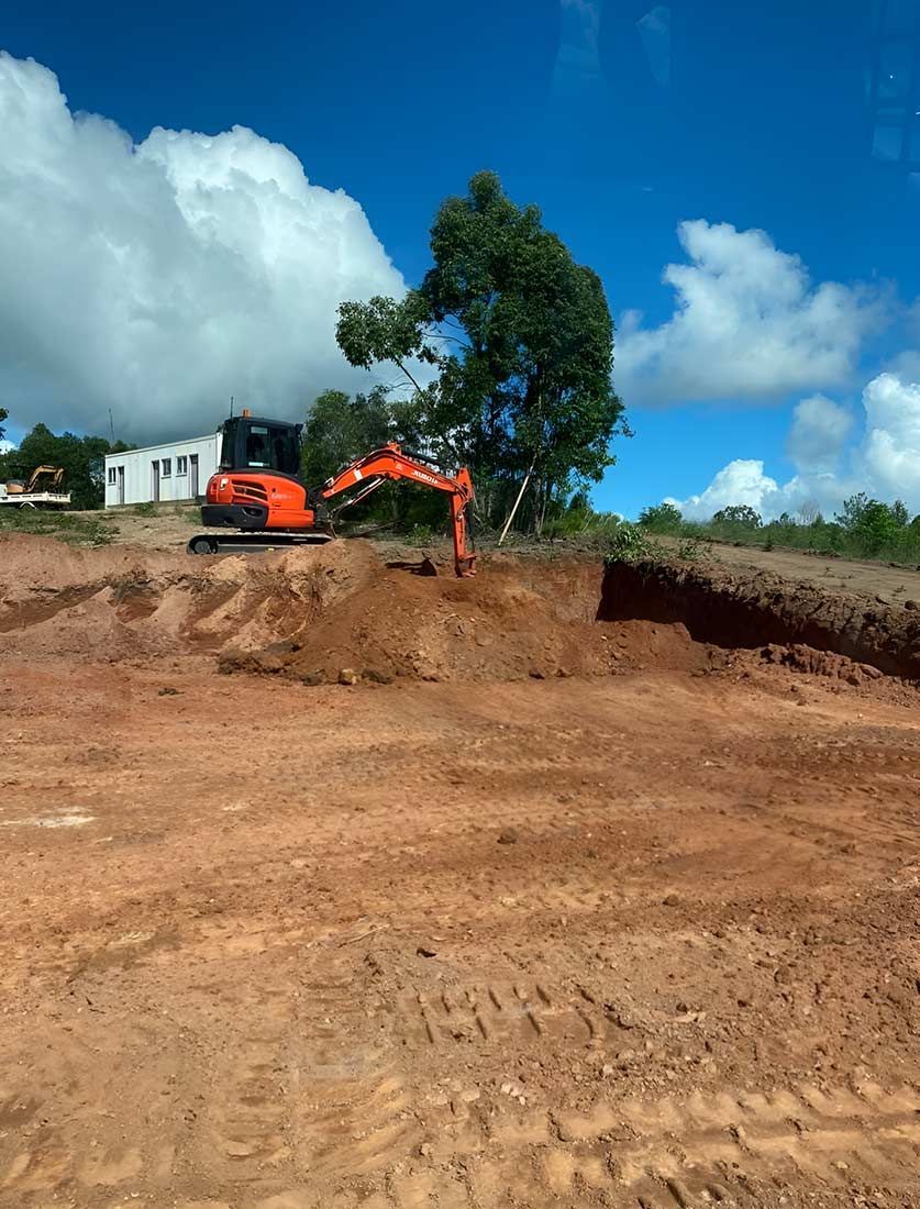 An Orange Excavator is Digging a Hole in a Dirt Field — Blue Gum Earthworks in Atherton, QLD