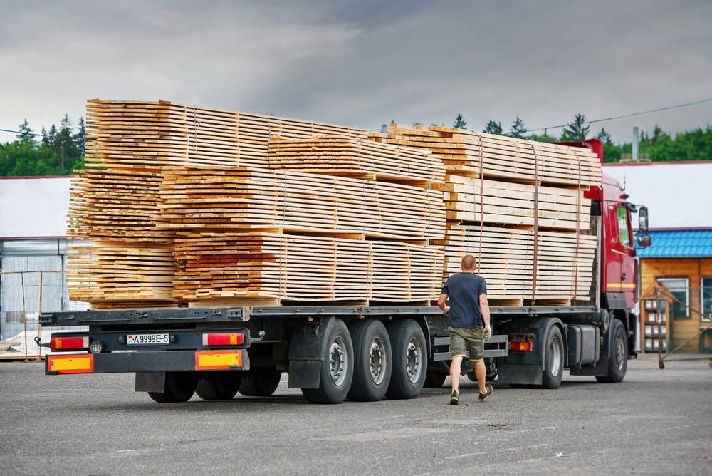 A Man is Standing Next to a Truck Carrying a Large Stack of Wood — Blue Gum Earthworks in Atherton, QLD
