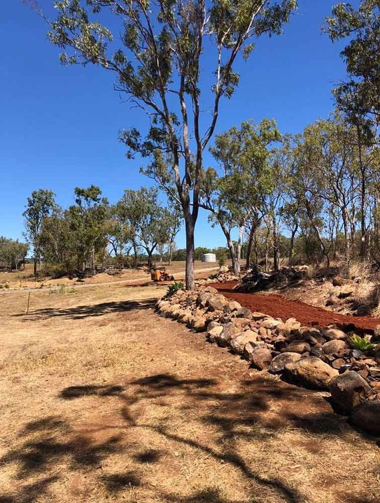 A Dirt Field With Trees and Rocks in the Foreground and a Blue Sky in the Background — Blue Gum Earthworks in Atherton, QLD