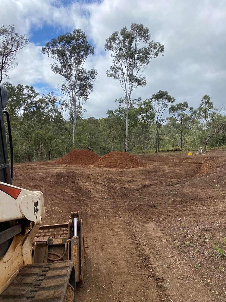 A Bulldozer is Driving Through a Dirt Field With Trees in the Background — Blue Gum Earthworks in Atherton, QLD