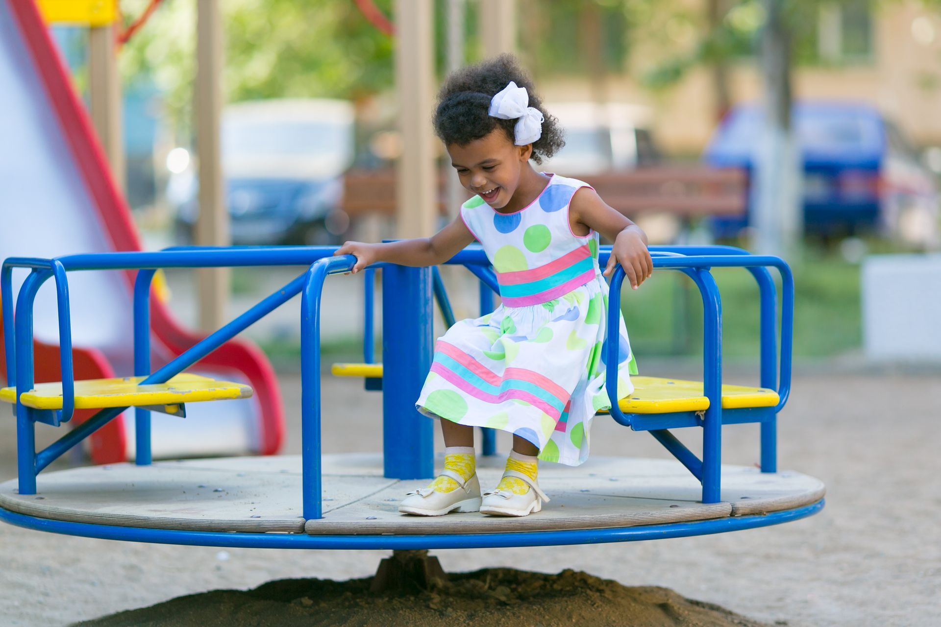 Child in a white dress riding a colorful playground merry-go-round outdoors