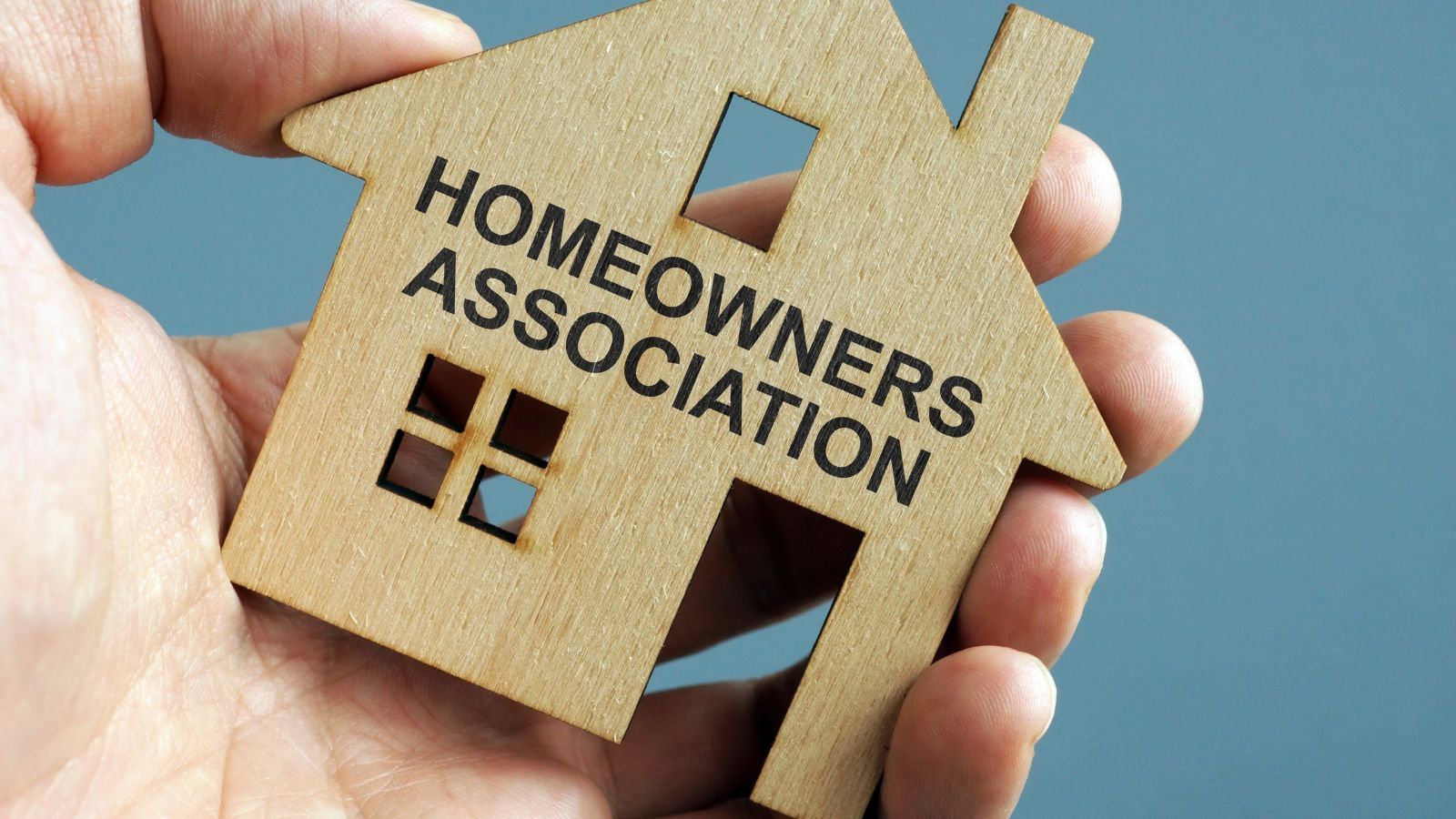 hand holding a wooden home that says homeowners association