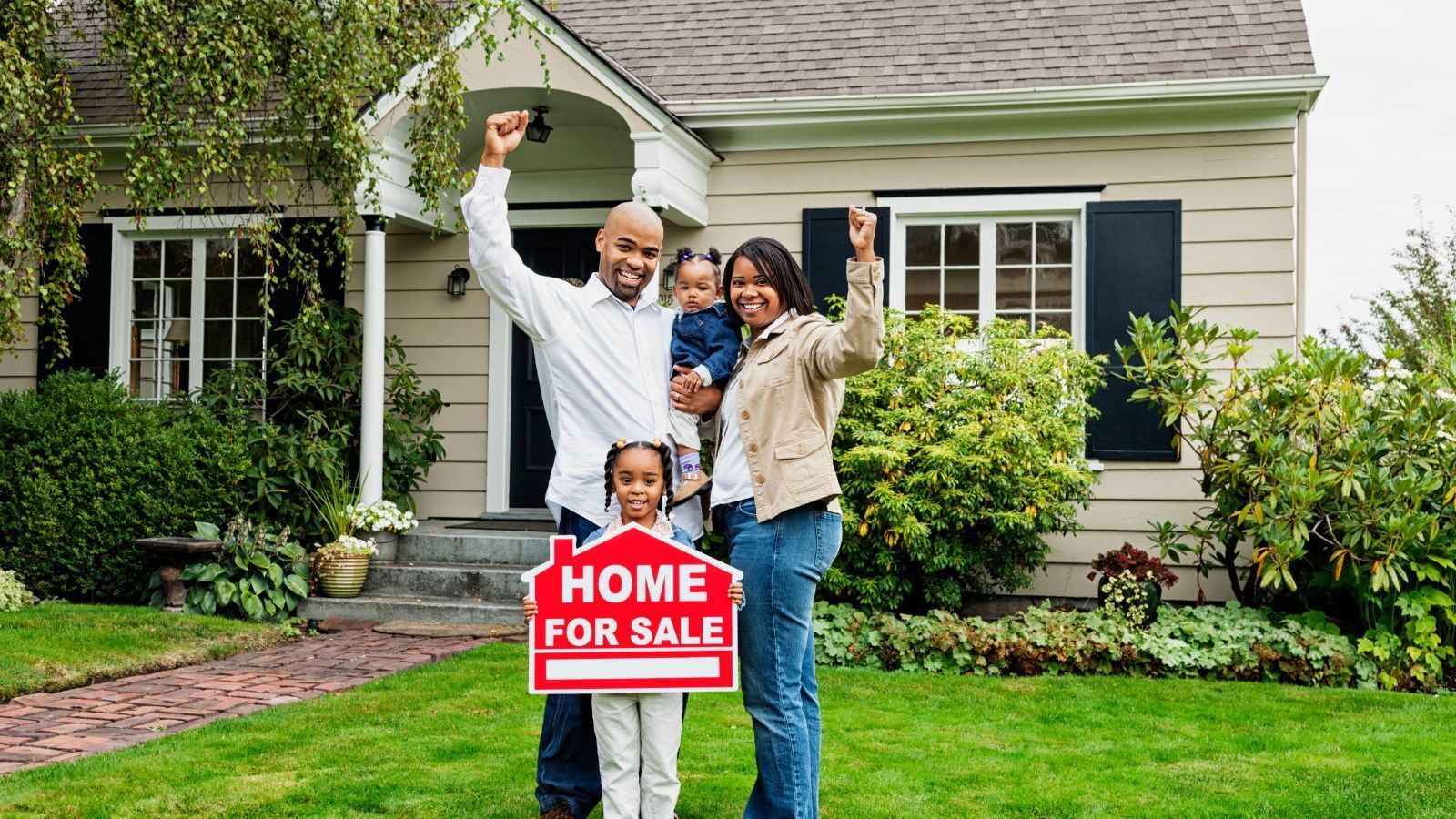 Family celebrating while holding a 'home for sale' sign