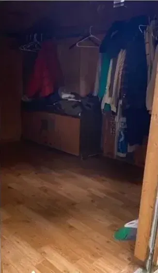 A room with a wooden floor and a closet with clothes hanging on the wall.
