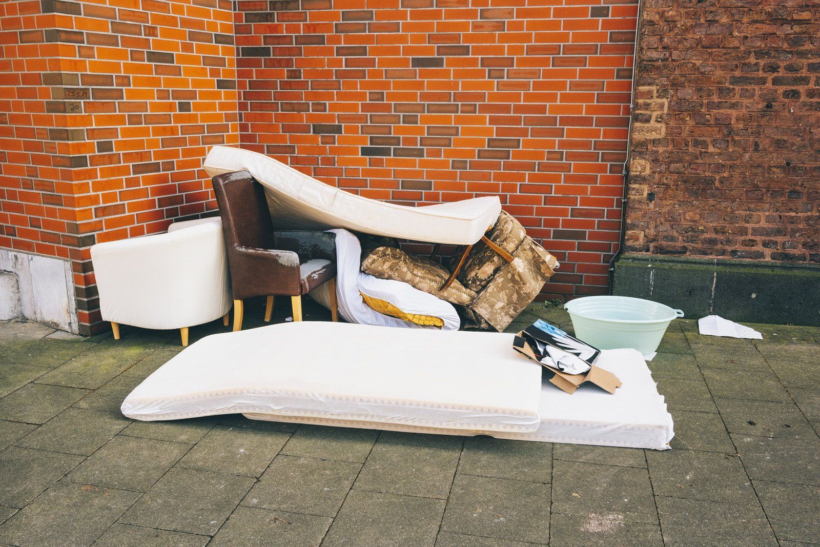 A pile of furniture is sitting on the sidewalk in front of a brick wall.