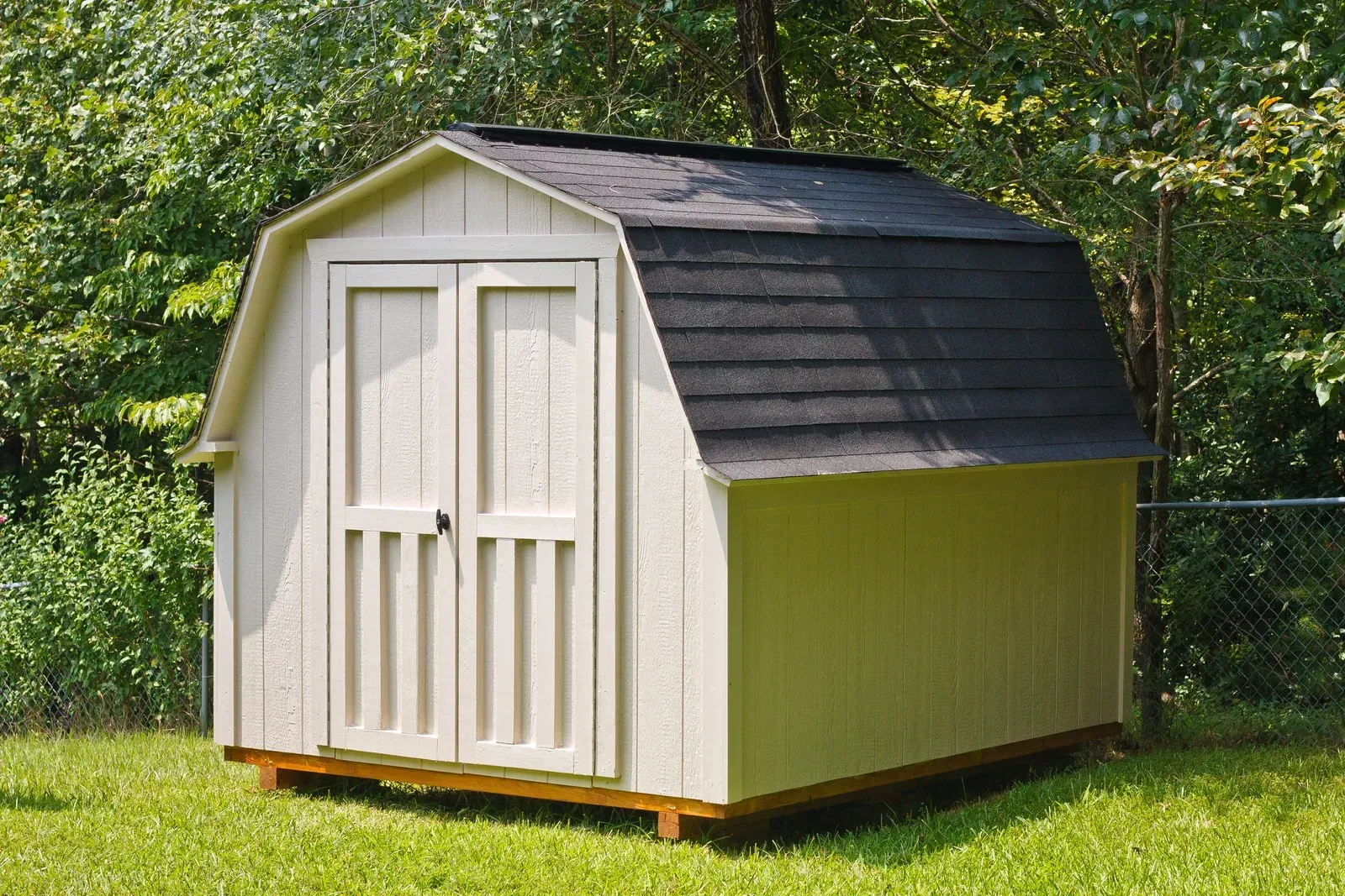 A white shed with a black roof is sitting in the grass.