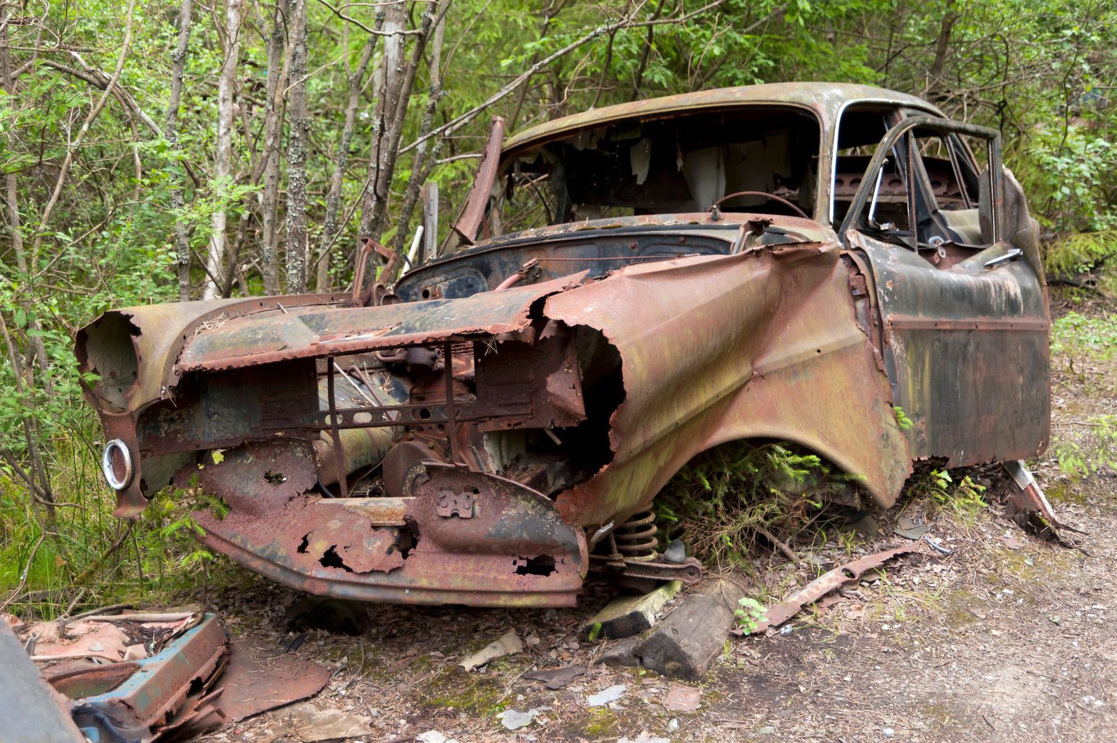 An old rusty car is sitting in the middle of a forest.