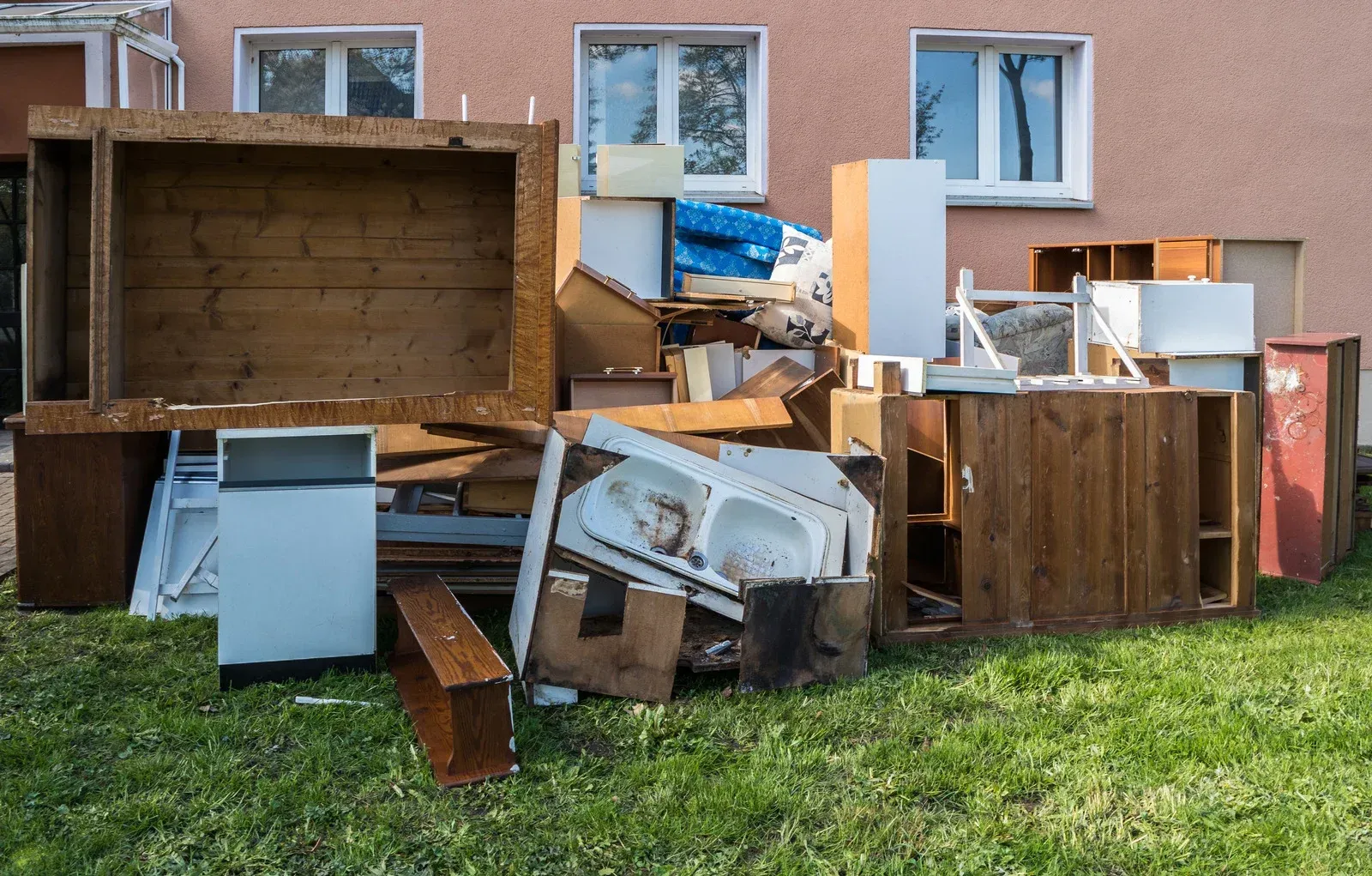 A pile of junk is sitting in the grass in front of a house.