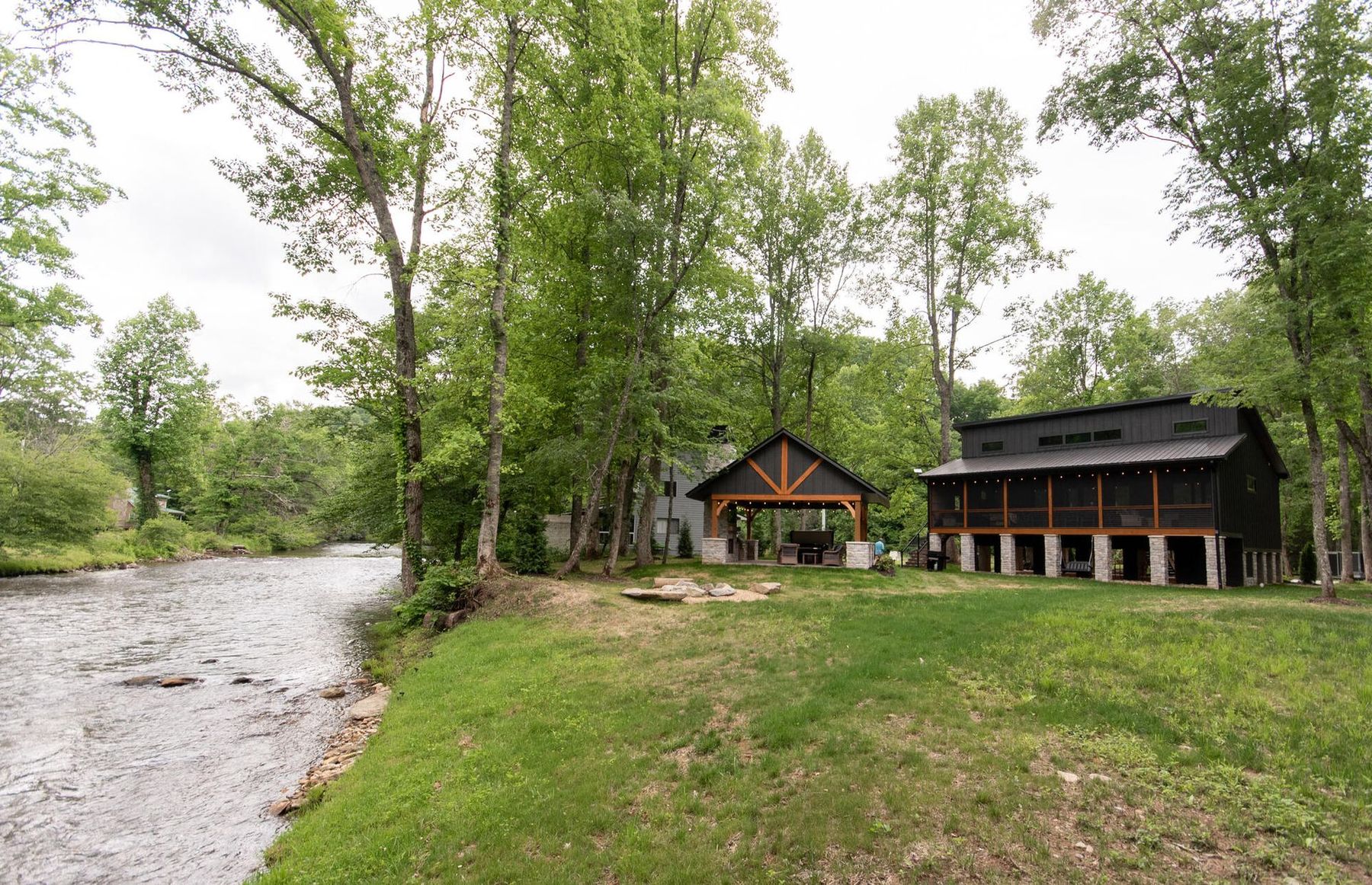White two-bay garage with covered side porches and large windows in a wooded setting