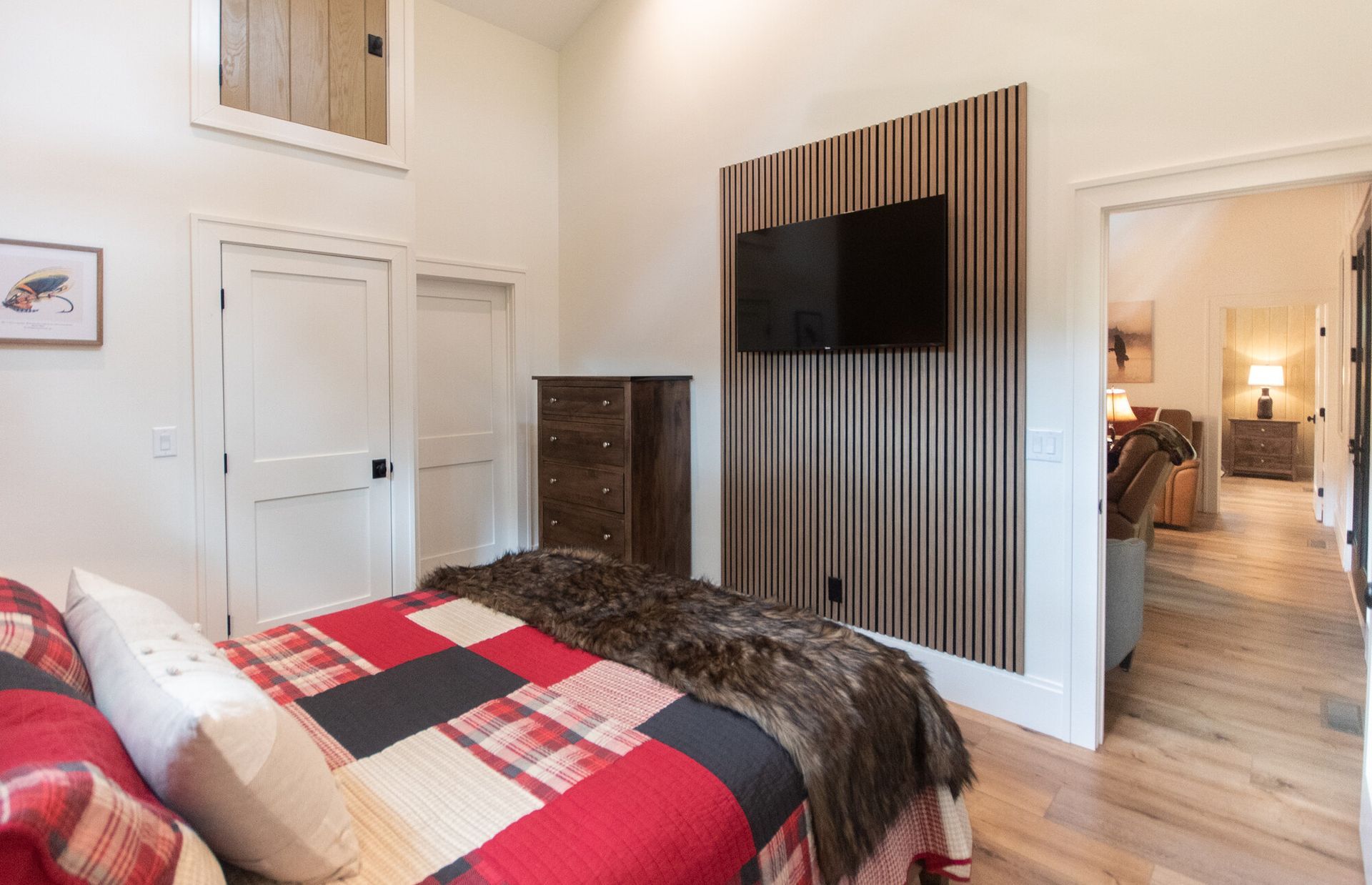 Bedroom with red plaid bedding, wall-mounted TV, striped accent wall, and open doorway to a hall