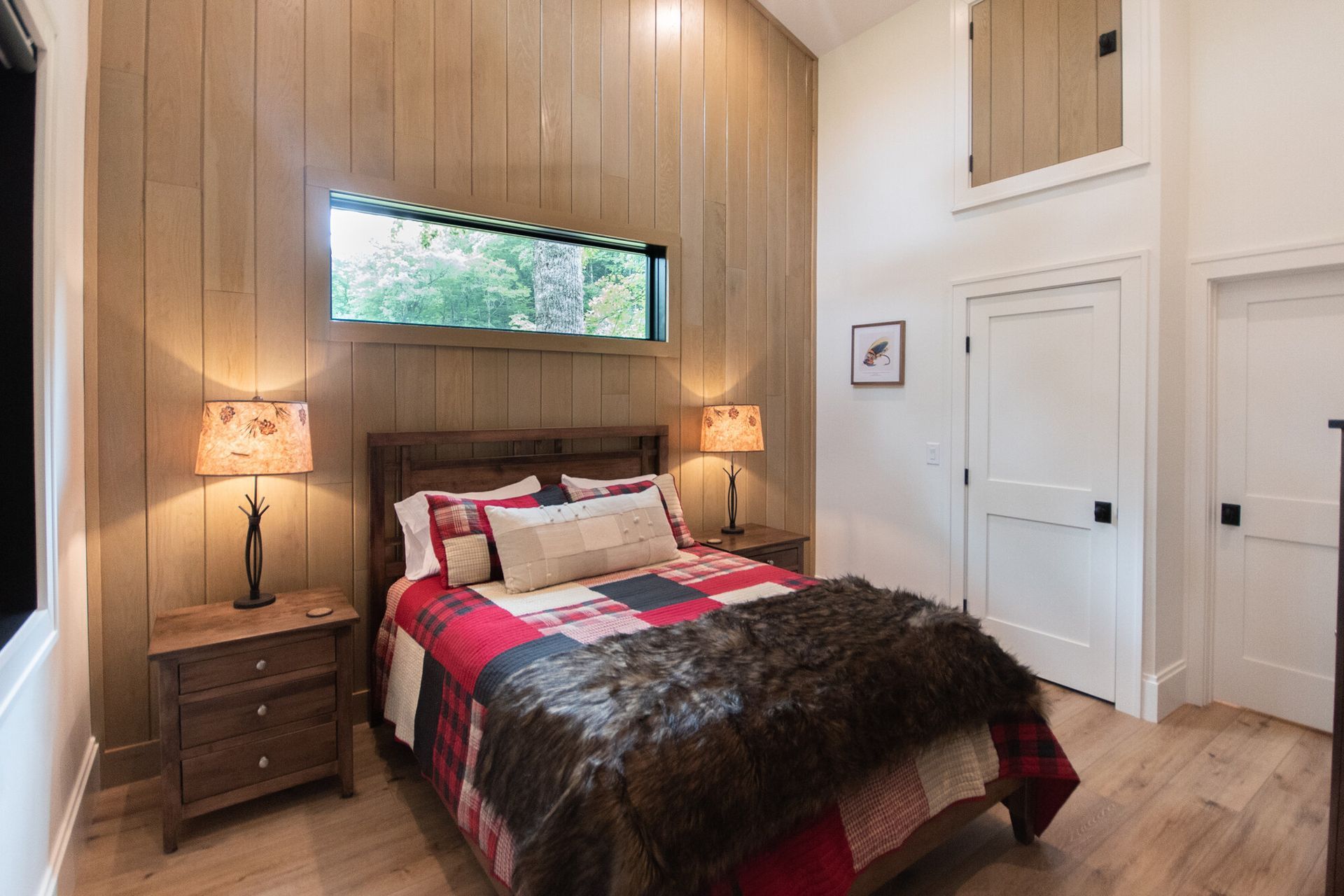 Modern bedroom with wood-paneled accent wall, bed with red and brown bedding, and two bedside lamps
