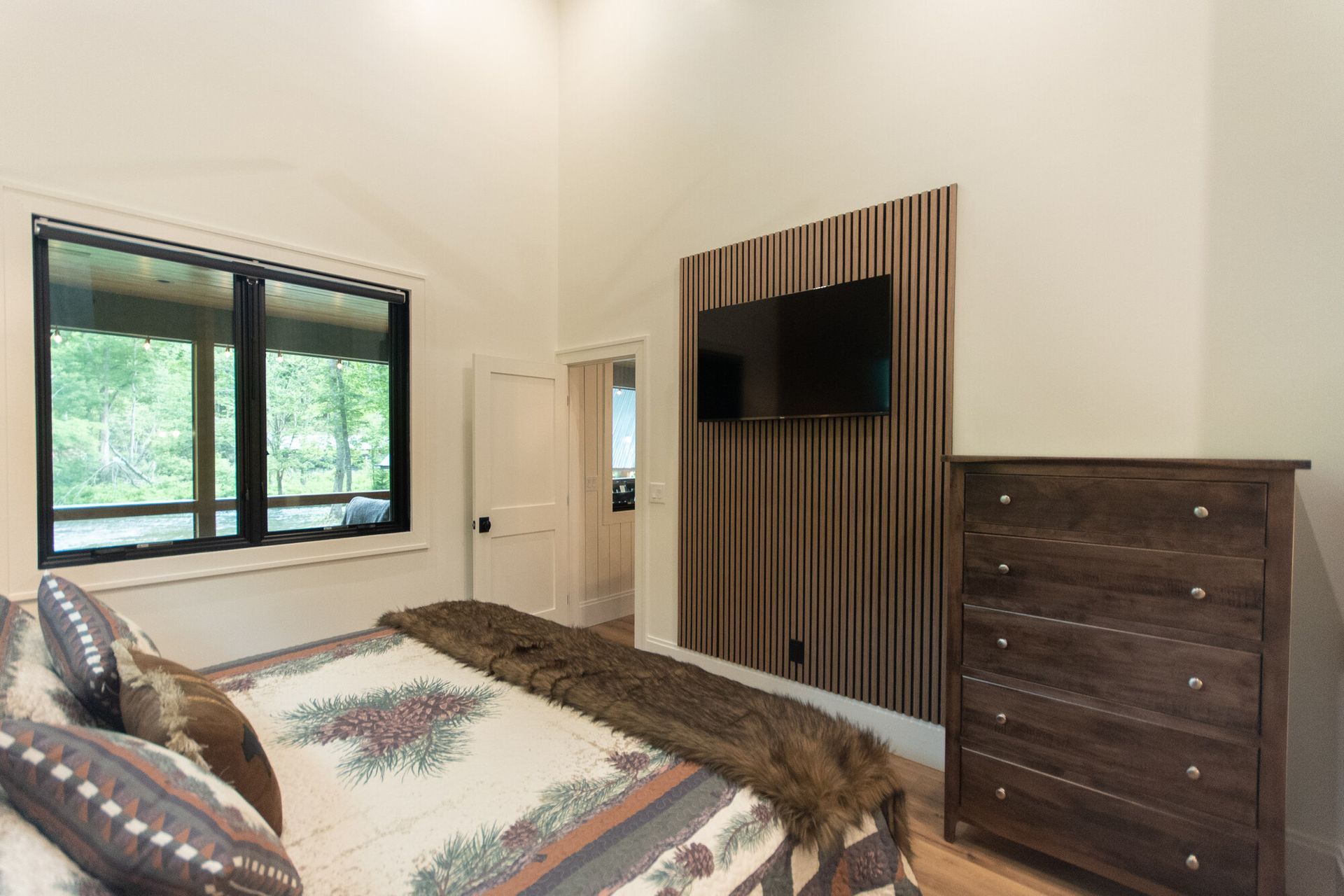 Bedroom with bed, wall-mounted TV, window, mirror, and dark wood dresser