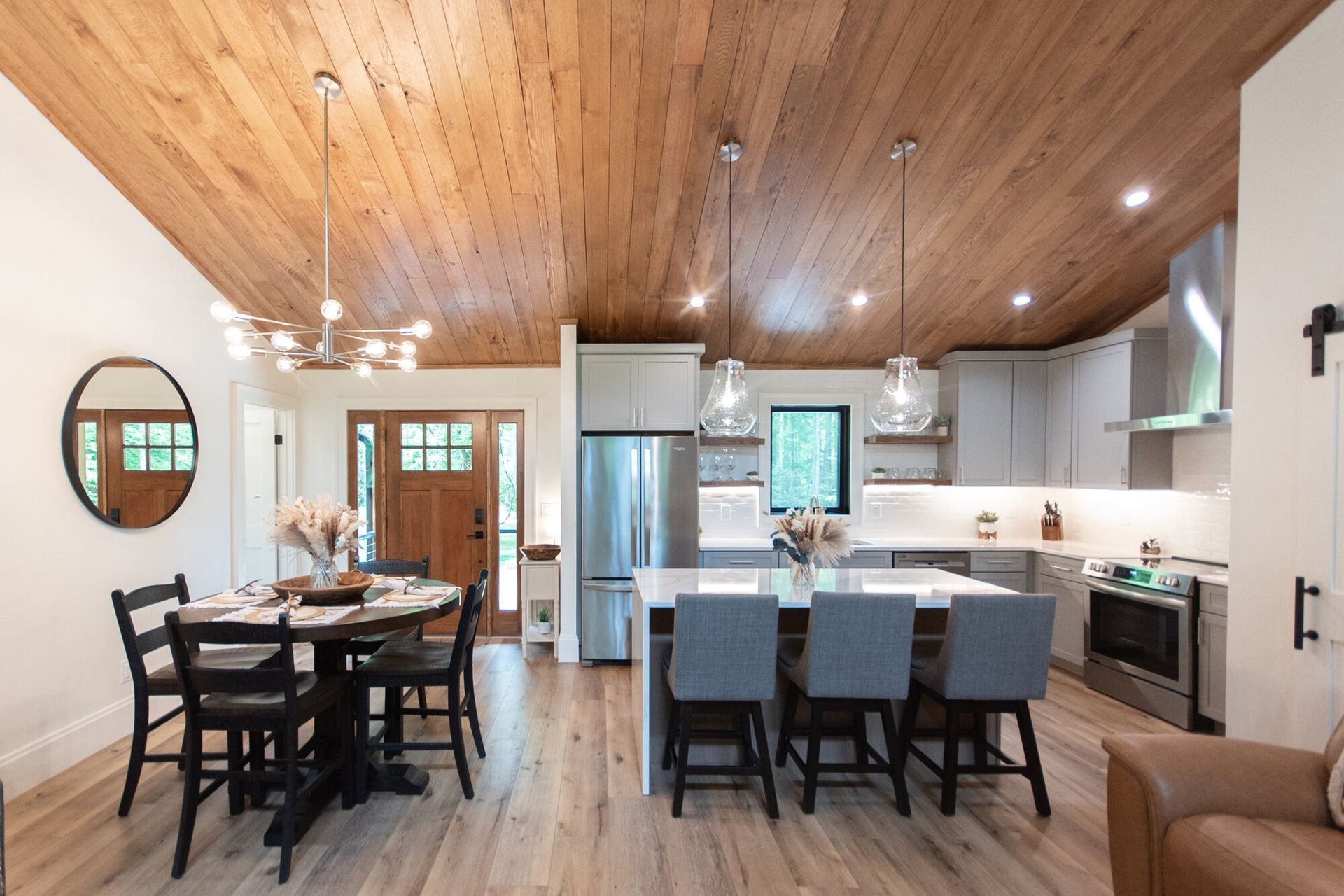 Modern open-concept kitchen and dining room with wood ceiling, island, stainless appliances, and dark dining table