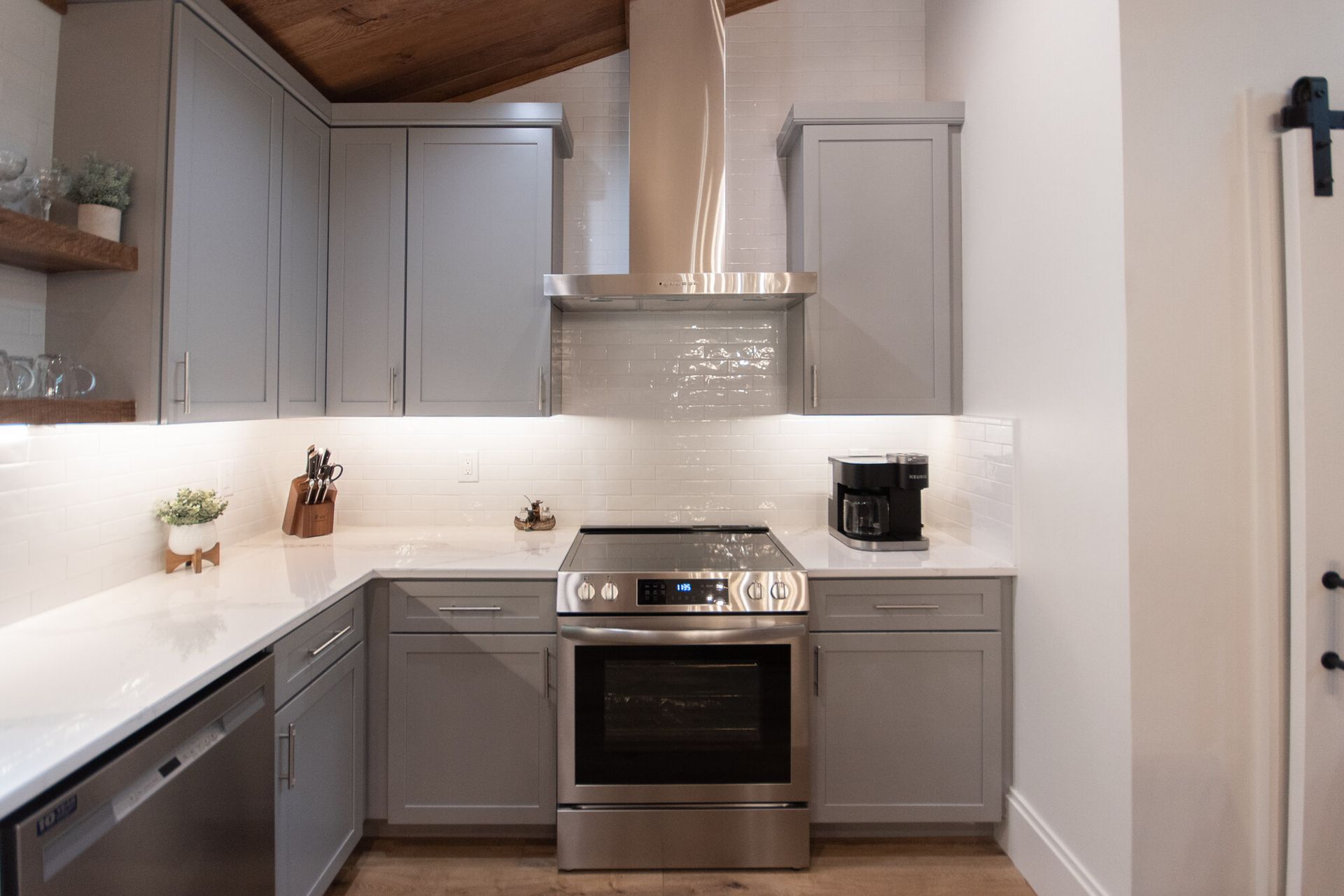 Modern kitchen with gray cabinets, white countertops, stainless stove, and wood ceiling