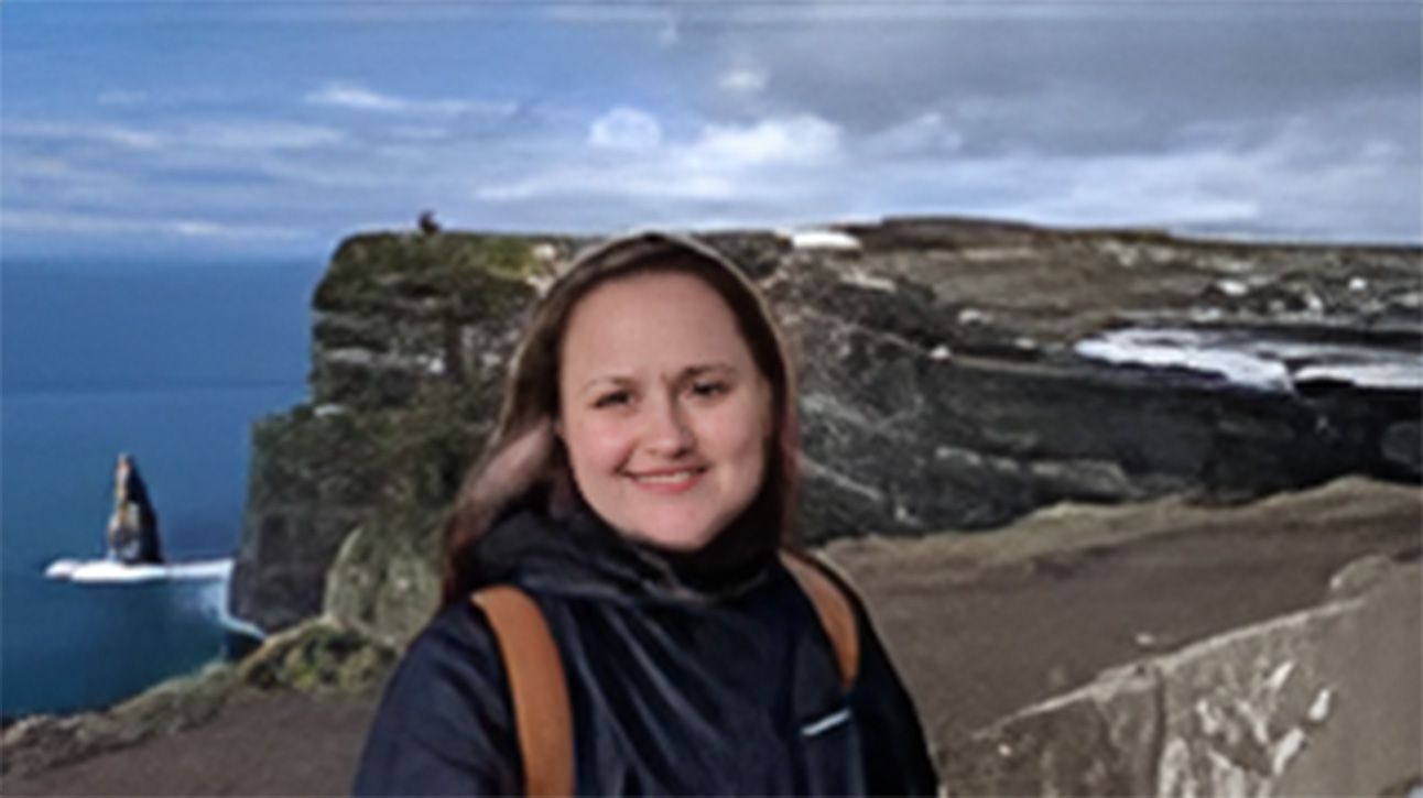 A woman is standing on top of a cliff overlooking the ocean.
