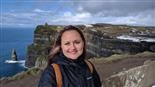 A woman is standing on top of a cliff overlooking the ocean.