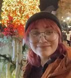 A woman with pink hair and glasses is smiling in front of a christmas tree.