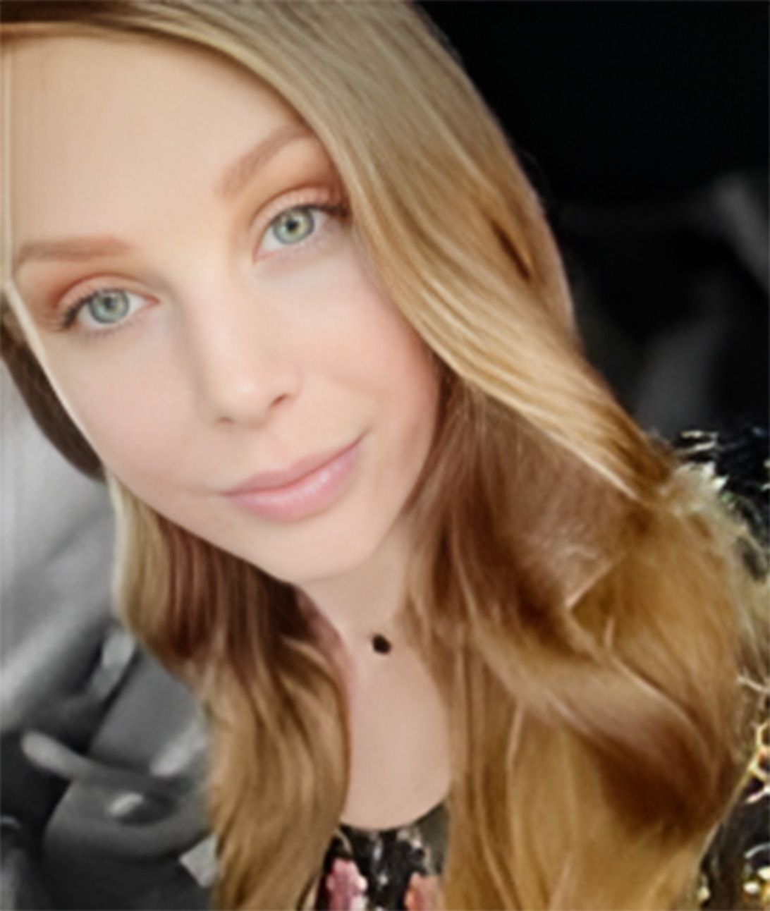 A woman with long blonde hair is taking a selfie in a car.