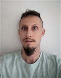 A man with a beard is taking a selfie in front of a white wall.
