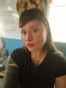 A woman is smiling in front of a wall of pink flowers.