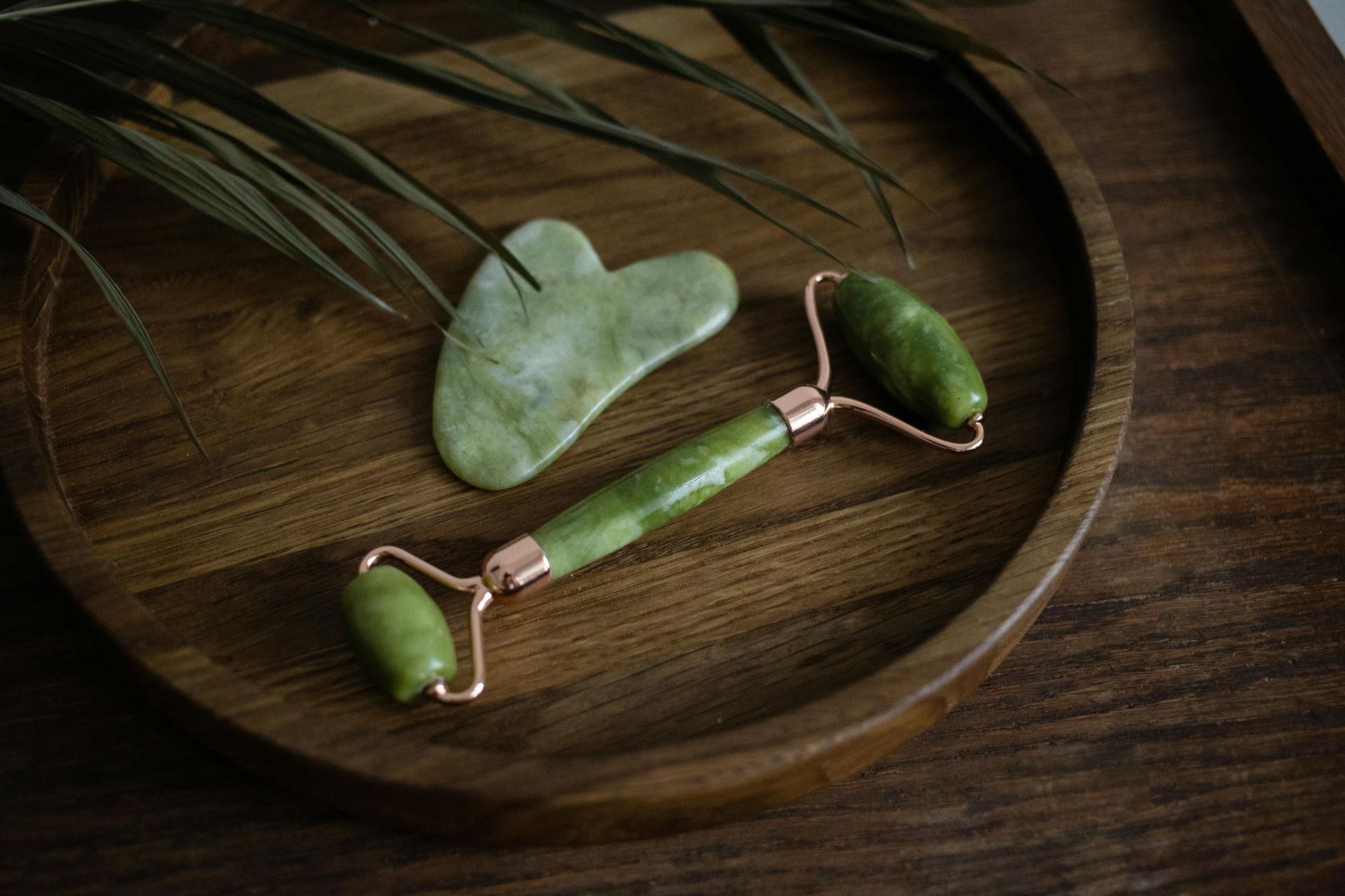 A jade roller and gua sha on a wooden tray.