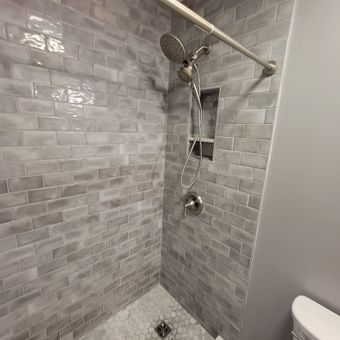 Tiled shower with rainfall showerhead, handheld wand, and built-in niche in a gray bathroom