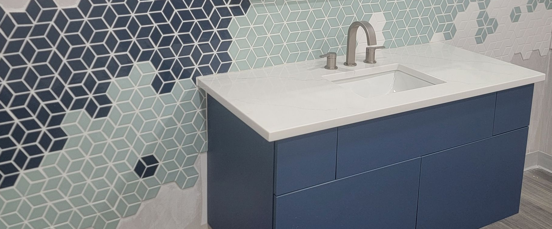 Blue vanity with white sink and faucet beside gray hexagon tile wall.