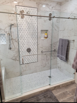 Modern tiled bathroom with a glass walk-in shower, white pebble floor, and hanging towels.