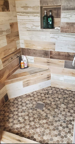Stone-tiled shower with built-in bench, niche shelves, and pebble floor in beige and brown tones