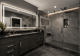 Modern bathroom with dark vanity, large mirror, and glass shower in gray tones