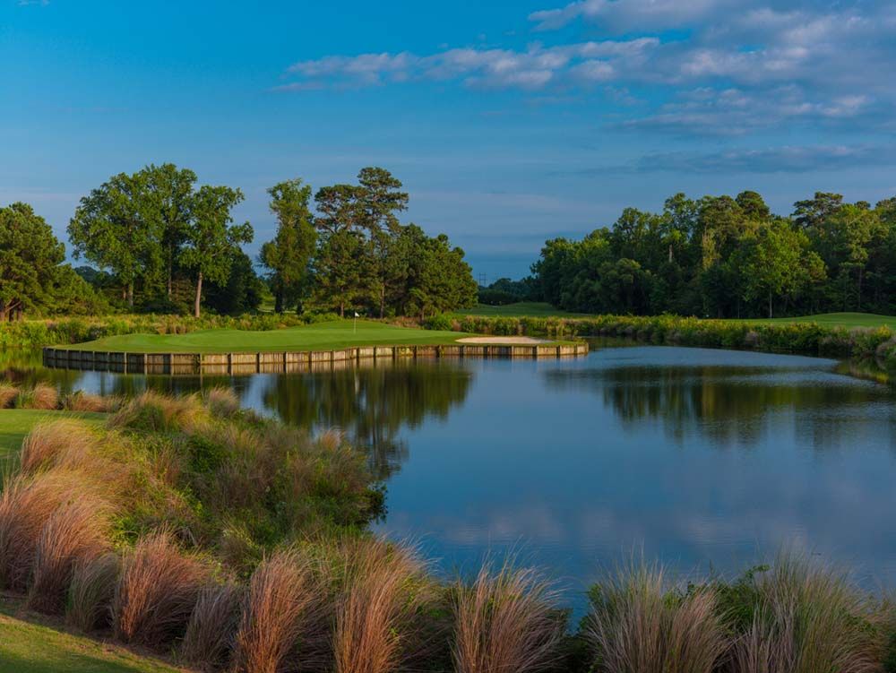 Scenic golf course with a pond reflecting the sky and surrounding trees.