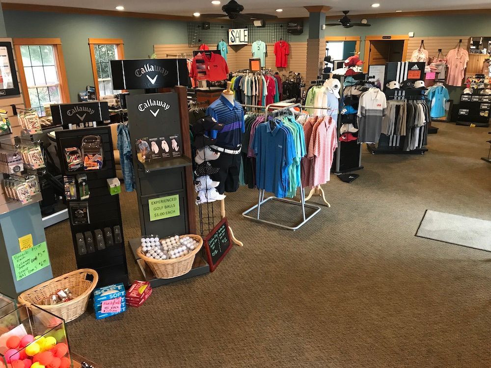 Interior of a golf pro shop with racks of clothing, shoes, and accessories. Callaway displays are prominent.