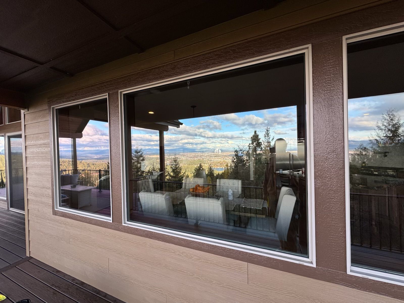 Three large windows with a view of a city and a dining table inside. Brown trim and beige exterior.