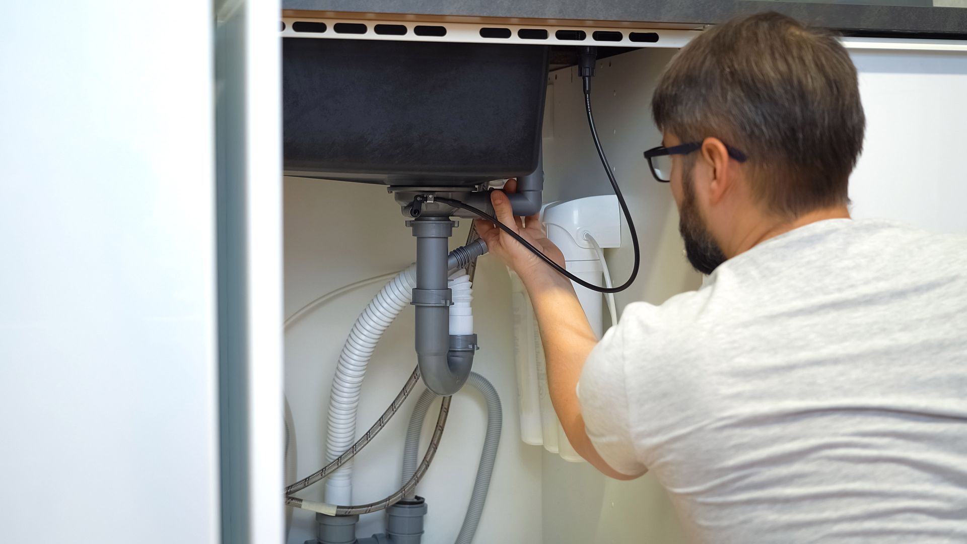 A man is fixing a sink in a kitchen.