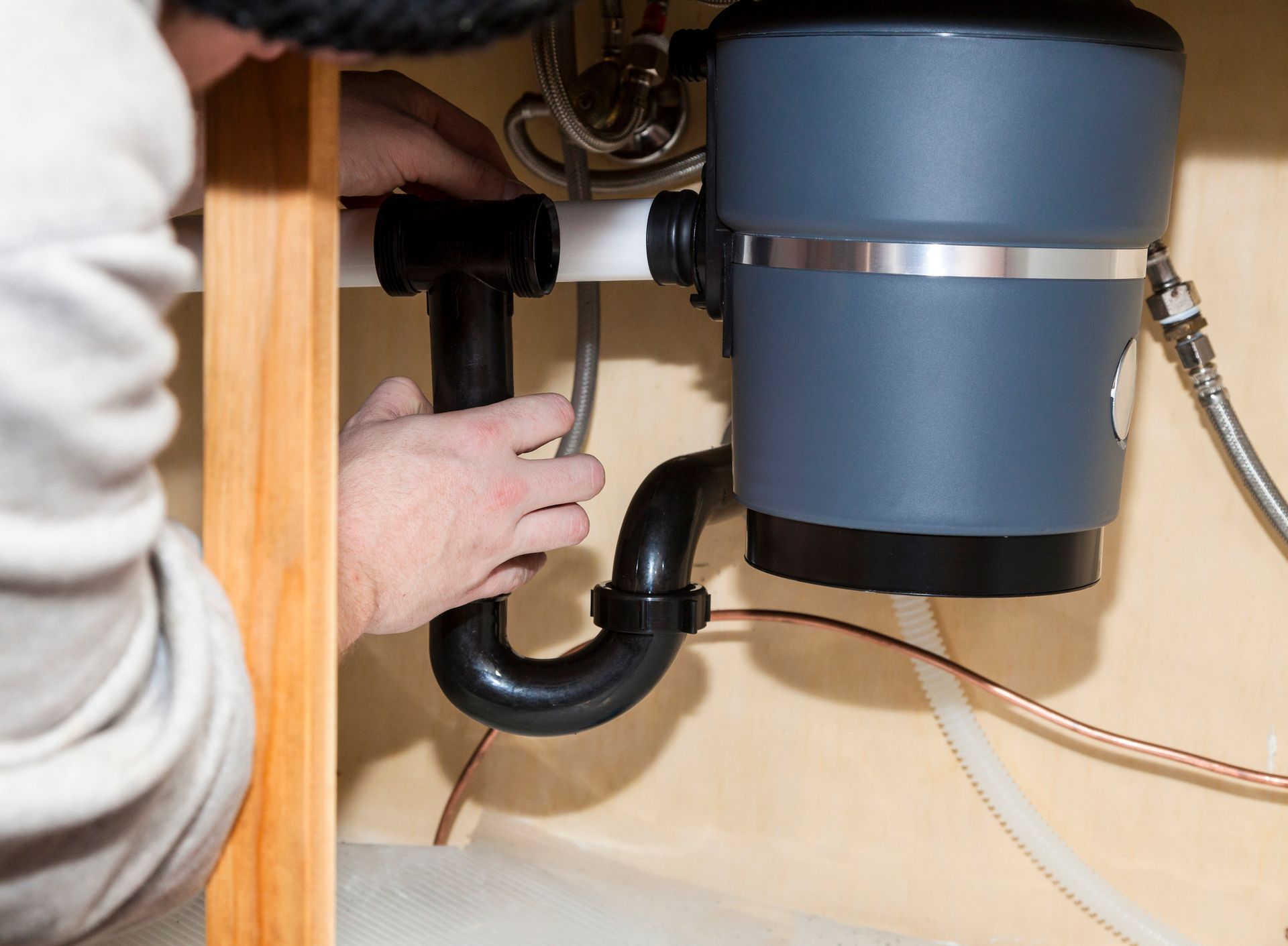 A person is fixing a garbage disposal in a kitchen sink.