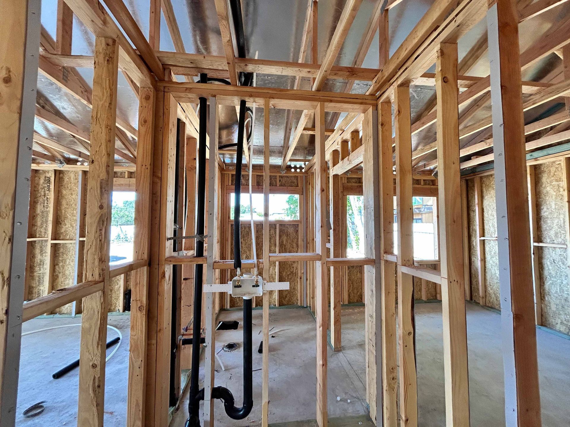 The inside of a house under construction with wooden beams and pipes.