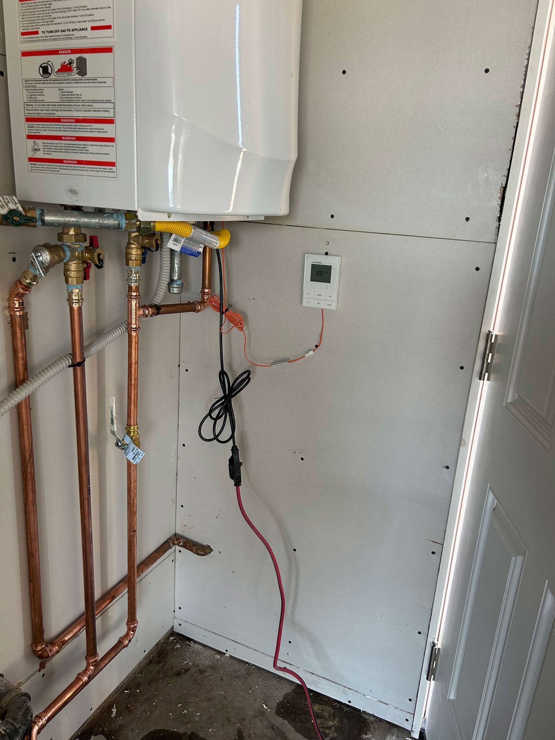 A room with a water heater and copper pipes on the wall.