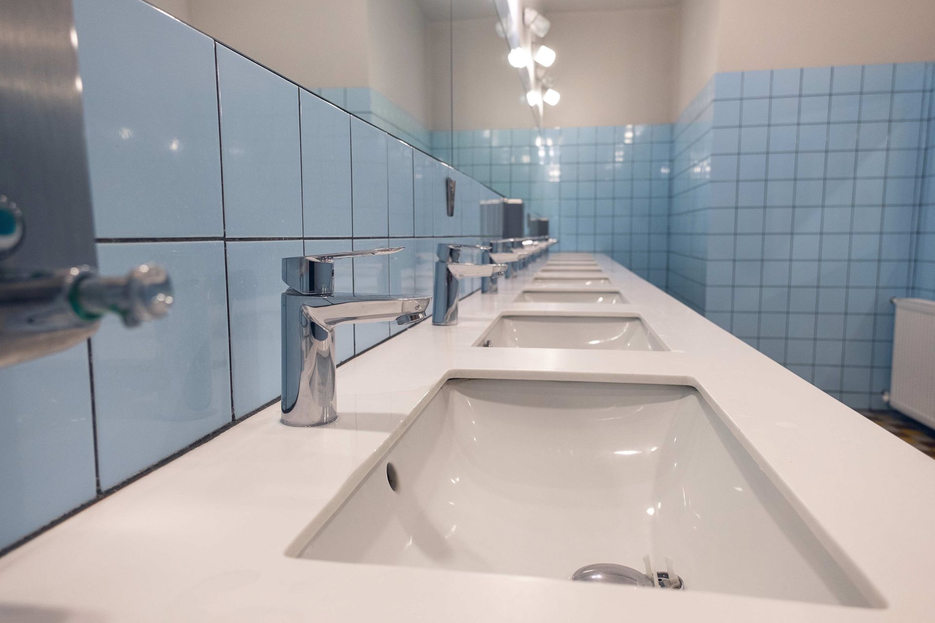 A row of sinks in a public restroom with blue tiles.