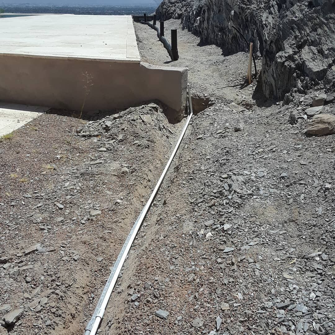 A metal pipe is laying in the dirt next to a concrete wall.