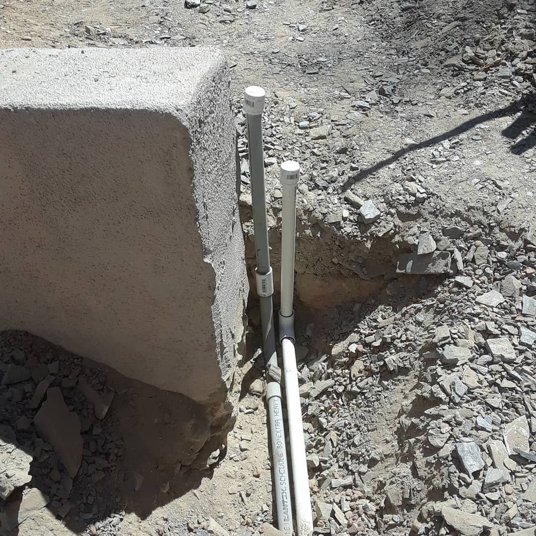 A pipe is sitting in the dirt next to a rock.