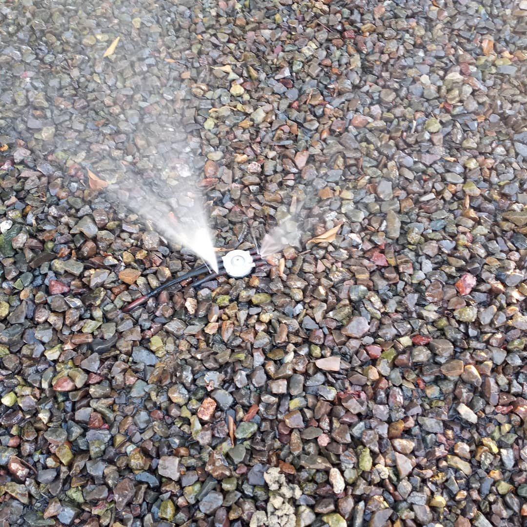 A sprinkler is spraying water on a pile of gravel.