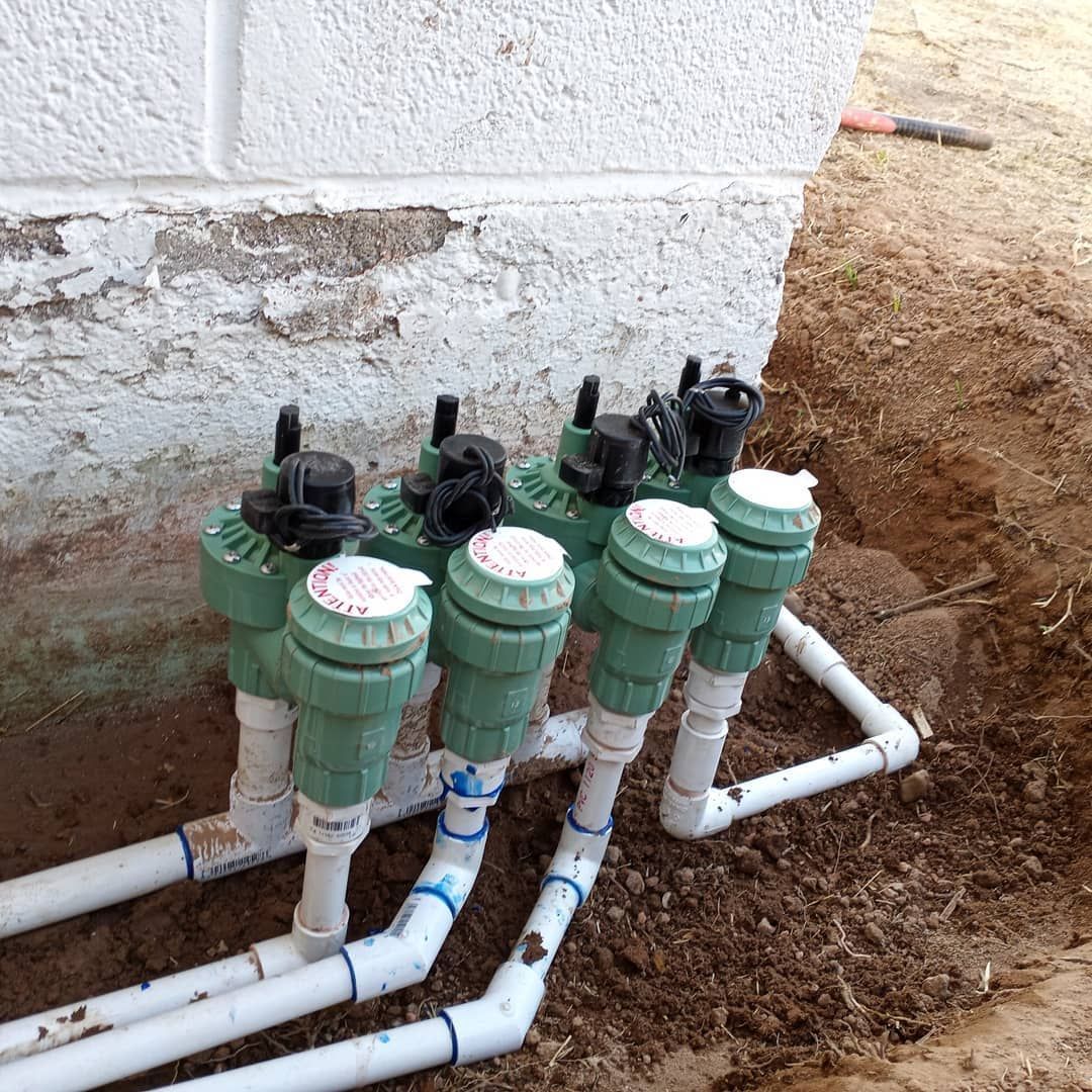 A row of green and white pipes are sitting in the dirt next to a brick wall.