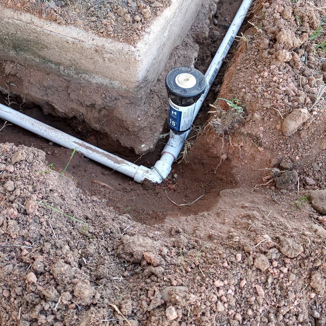 A sprinkler is sitting in the dirt next to a pipe.