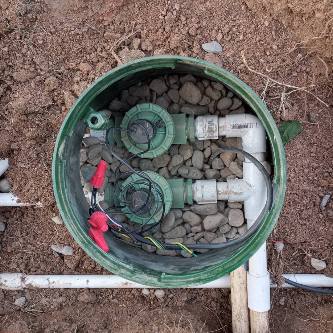 A green bucket filled with rocks and pipes is sitting in the dirt.